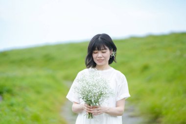 Beyaz elbiseli, orta boylu saçlı bir kadın açık gökyüzünün altındaki bir dağ yolunda tek başına dururken bebek nefesi tutuyor, bina yok. Nagano Bölgesi, Kirigamine, Japonya, yaz.