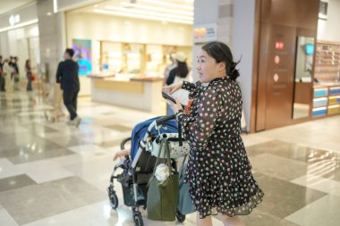 Bir alışveriş merkezinin otoparkında Çinli bir aile arabalarının yanında yürürken bir yaşındaki bir bebek bebek bebek arabasında otuzlu yaşlarında bir anne tarafından nazikçe ve güvenli bir şekilde itiliyor. Bahar. Şangay 'da. Çin.