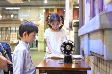 Eski bir alışveriş merkezinde, Çinli bir aile günün tadını çıkarıyor: bebek arabasındaki bir yaşındaki bir çocuk, otuzlu yaşlardaki yetişkinler gibi 10 yaşın altındaki çocuklar gülüyor ve sohbet ediyorlar klasik dikiş makinesi kullanıyorlar. Şangay, Çin. Bahar.