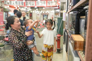 Eski bir alışveriş merkezinde, Çinli bir aile günün tadını çıkarıyor; bir yaşındaki bir çocuk bebek arabasında ve on yaşın altındaki çocuklar otuzlu yaşlardaki yetişkinler eski televizyonları izlemek için toplanırken sohbet ediyorlar. Şangay, Çin. Bahar.