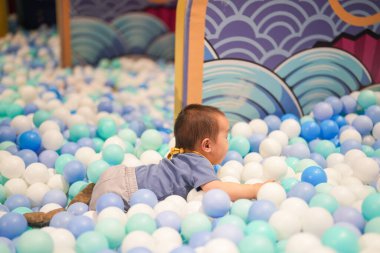 Kapalı bir oyun alanında, bir yaşındaki Çinli bir bebek plastik top havuzunda yüzer gibi oynuyor. Hongkou Bölgesi, Şangay, Çin. Bahar.