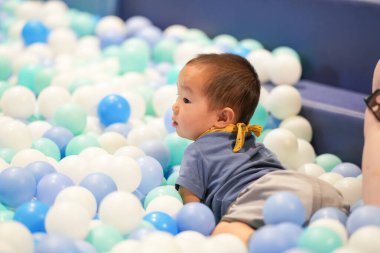 Kapalı bir oyun alanında, bir yaşındaki Çinli bir bebek plastik top havuzunda yüzer gibi oynuyor. Hongkou Bölgesi, Şangay, Çin. Bahar.