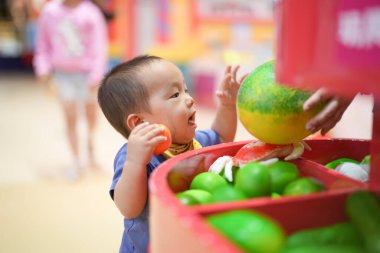 Çinli bir bebek süpermarkette sepetle alışveriş yapmaktan ve kapalı alanda oyun oynamaktan hoşlanır. Hongkou Bölgesi, Şangay, Çin. Bahar.