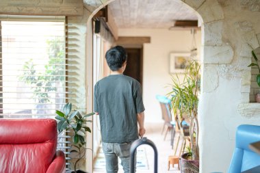In a Mediterranean-style living room, a Japanese man in his 30s sprays water on a houseplant. Summer. Japan.