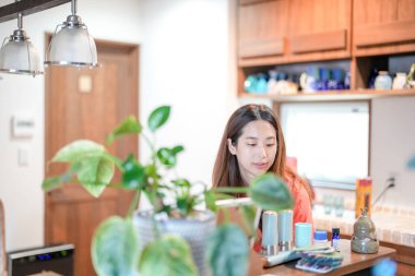 In a Mediterranean-style dining kitchen, a Japanese woman in her 20s wearing an orange shirt is cleaning the table. Summer. Japan.