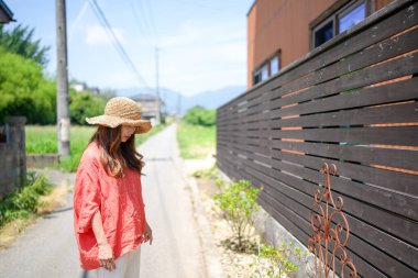 A woman in a red shirt and straw hat is standing on a street. The street is empty and the sky is clear