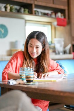 A woman in an orange shirt is sitting at a table with a book and two glasses of water. She is smiling and she is enjoying her time