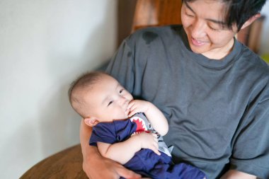 A man is holding a baby in his arms. The baby is wearing a shirt with a shark on it
