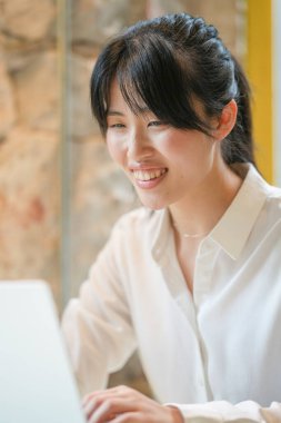 A woman is sitting at a table with a laptop in front of her. She is smiling and she is enjoying herself