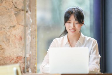 A woman is sitting at a table with a laptop in front of her. She is smiling and she is enjoying her work