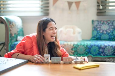 A woman is sitting on a couch and laughing while playing with a train set. The train set is on a table in front of her
