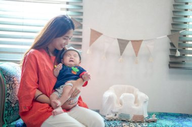 A woman is holding a baby in her arms. The baby is wearing a hat and a blue shirt