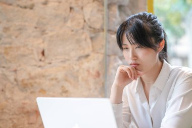 A woman is sitting at a table with a laptop in front of her. She is frowning and looking at the screen