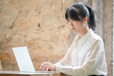 A woman is sitting at a table with a laptop in front of her. She is typing on the keyboard and she is focused on her work. Concept of productivity and concentration