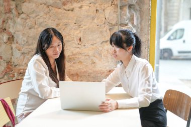 Two women are sitting at a table with a laptop in front of them. They are discussing something important