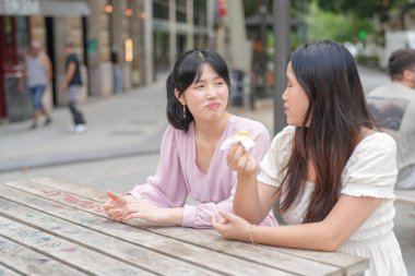Two women sitting at a table eating food. One of them is holding a piece of food in her hand