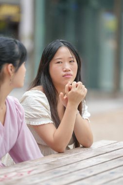 Two women sitting at a table, one of them is wearing a white shirt. The woman in the white shirt is looking down and she is in a contemplative mood