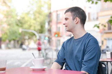 Bir adam önünde bir fincan kahveyle bir masada oturuyor. Mavi bir gömlek giyiyor ve kahvesinin tadını çıkarıyor. Sahne birkaç kişiyle birlikte bir sokakta geçiyor.