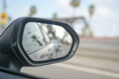 A car's rear view mirror shows a reflection of a motorcycle. The motorcycle is in the foreground and the car is in the background. The mirror is clean and clear