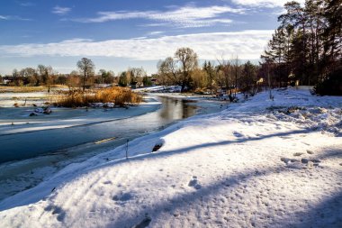 Kışın donmuş nehir, kar ve bulutlu mavi gökyüzü..