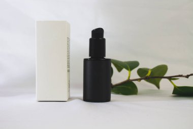 Siyah şişenin ve beyaz doğal kozmetik kutusunun beyaz arka planda, kamelya çiçekli, yatay fotoğraf, maketler için.