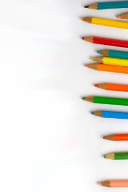Çocukların renkli kalemleri, görüntünün sağındaki beyaz sayfanın üzerine düşerek sıra oluşturur. Okula dönmek için fotoğraf, arka plan olmadan, metin için yer bırakılır.