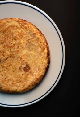 Mükemmel pişirilmiş lezzetli bir İspanyol omletinin yakın plan bir portresi. Restoran ortamında servis ediliyor. Bu geleneksel yemek ağız sulandırıcı bir yumurta, patates ve soğan karışımı içeriyor. Tat alma duyunuzu tatmin etmek için ustalıkla hazırlanmış.