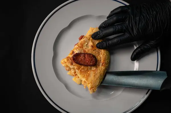 Geleneksel İspanyol omletinin yakın plan bir portresi. Kırsal seramik tabakta leziz domuz eti dilimleri servis ediliyor. Omletin altın-kahverengi kabuğu, Chorizo 'nun canlı kırmızı renkleriyle çok güzel zıtlaşır ve büyüleyici bir görsel disk oluşturur.