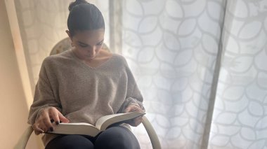 Kitap Günü 'nün özünü yakalayın. Bir kız en sevdiği kitabın sayfalarında teselli bulur. Sandalyede nazikçe sallanırken. Okumaya dalmış, edebiyatın coşkusunu ve mucizesini somutlaştırıyor, izleyicileri hikaye anlatmanın büyüsünü benimsemeye çağırıyor..