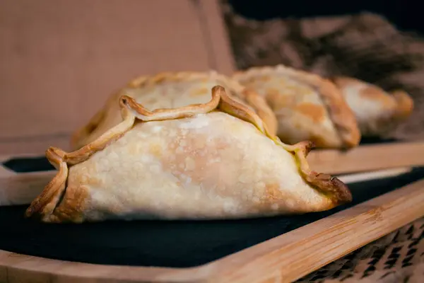 Indulge in the authentic flavors of Argentina with our delicious empanadas, elegantly presented on rustic wooden boards against a warm cardboard background. Each bite is a journey through the vibrant culinary heritage of Argentina, perfect for adding