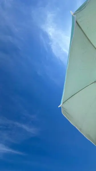 A serene moment captured from the perspective of someone lying on a beach towel, looking up at the clear blue sky. The beach scene is tranquil, with the soft sand and gentle waves in the background, evoking a sense of relaxation and calmness