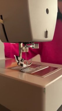 Bir dikiş makinesinin yanına yerleştirilmiş düz kapalı dikiş makinesi iğnesi, evde dikiş dikmeyi öğrenen genç bir kadının bir anını yakalıyor. DIY projeleri, ev dikimi ve yaratıcı hobiler için mükemmel.
