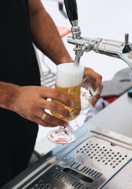 Bu resimde bir barmen mükemmel bir bira bardağını doldururken görülüyor. Bira musluktan bir bardağa akar ve kalın, kremsi bir kafa oluşturur. Barmenin hünerli tekniği dengeli bir dökümü garantiler ve özünü yakalar.