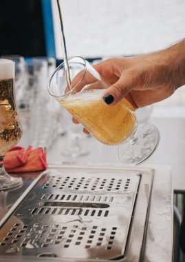 Bu görüntüde bir barmen, titremeyen bir elle bardağa bira dolduruyor. Bira, altın sıvıyı ve köpüklü kafayı bardakta oluştururken gösteriyor. Barmenin benzersiz siyah tırnak cilası sosyeteye yeni bir tarz katıyor.