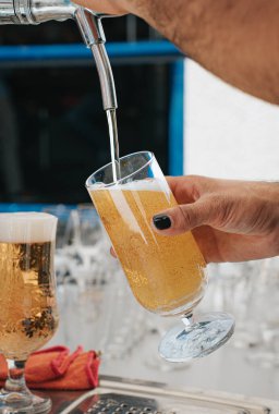 Bu resim bir barmeni bardağa bira dökerken ustalıkla yakalıyor. Altın sıvı musluktan pürüzsüzce akar ve camların üzerinde köpüklü bir kafa oluşturur. Barmenlerin eli, süslenmişti.