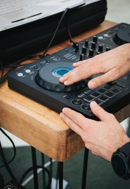 Bu yakın plan görüntü, bir açık hava etkinliği sırasında ses mikserini çalıştıran bir DJ 'in ellerine odaklanıyor. DJ 'in elleri karıştırıcının kontrolünü ustalıkla ayarlıyor, hassasiyeti vurguluyor ve...