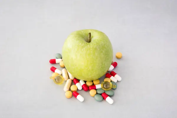 green apple with a pile of medicines next to it