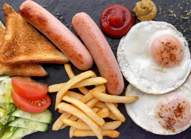 Koyu panoda kahvaltı, salata, yumurta, sosis, patates kızartması ve tost. Üst görünüm