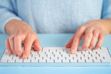 Female typing text on white keyboard on blue background. Close up