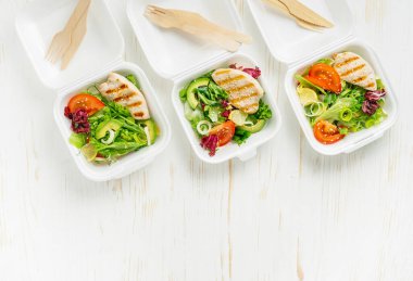 Lunch boxes with salad and grilled chicken on white wooden background. Copy space