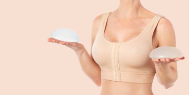 Woman wearing a compressing bra after breast augmentation surgery and holding implants in hands. Copy space clipart