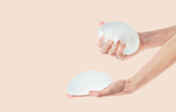 Female hands holding and squeezing soft round breast implants. Plastic surgery, copy space