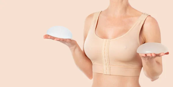 Göğüs büyütme ameliyatından sonra sutyen takan ve ellerinde implantlar tutan bir kadın. Boşluğu kopyala