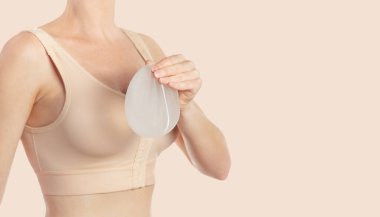 Göğüs büyütme ameliyatından sonra sutyen takan ve implantı elinde tutan bir kadın. Boşluğu kopyala