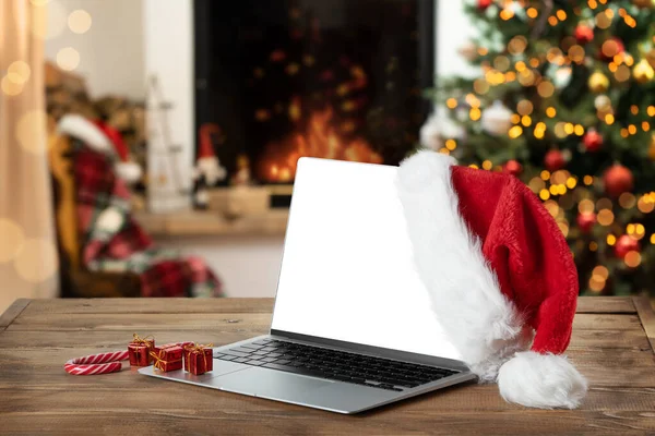Laptop with blank screen on rustic Christmas background interior with fireplace. Christmas online shopping.