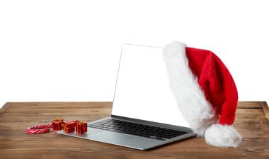 Beyaz beyaz ekranlı dizüstü bilgisayar ve ahşap kırsal masada Noel Baba şapkası. Kesme yolu. 