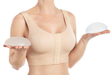 Woman wearing a compressing bra after breast augmentation surgery and holding implants in hands isolated on white background with clipping path. clipart