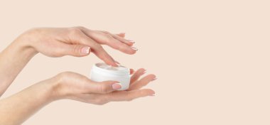 Bej arka planda kozmetik krem kavanozu tutan bir kadın. Boşluğu kopyala, kapat