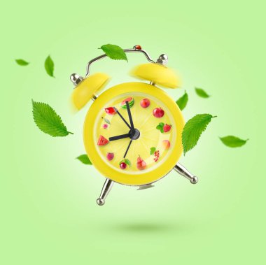 Yeşil zemin üzerinde meyve ve uçan yapraklar olan sarı alarm saati. 