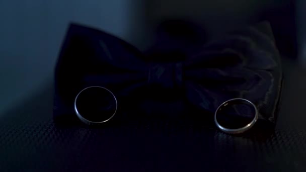 Два Обручальных Кольца Лежат Галстуке Бабочке Освещены Ярким Лучом Света — стоковое видео